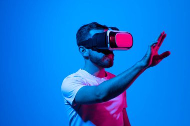 Heyecanlı sakallı bir adam sanal gerçekliği VR kulaklığıyla yaşıyor ve önünde gördüğü bir şeye elleriyle dokunuyor. Metaverse ve oyun.