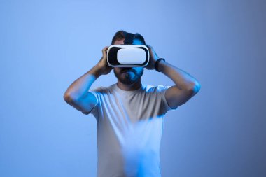 VR gözlüklü genç sakallı adam havaya dokunuyor ve karanlık neon ışıklardaki yeni duygularla heyecanlanıyor..