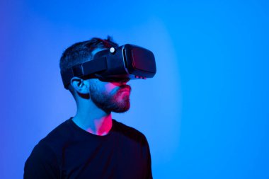 Sanal gerçeklik dünyası. VR kulaklıklı sakallı adam, arkadaşlarıyla metaevrende video oyunu oynarken bir şeye dokunuyor, neon ışığı altında duruyor..