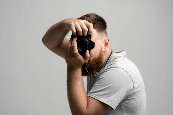 Fotógrafo homem bonito e confiante com uma grande câmera dslr profissional tirando fotos no fundo branco. — Fotografia de Stock