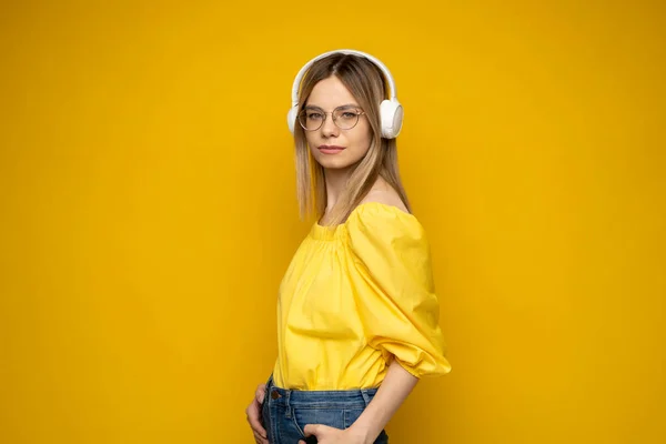 Linda chica joven en camiseta amarilla escuchar música con auriculares y posando aislado sobre fondo amarillo de la pared. Gente emociones concepto de estilo de vida. Simular espacio de copia. —  Fotos de Stock