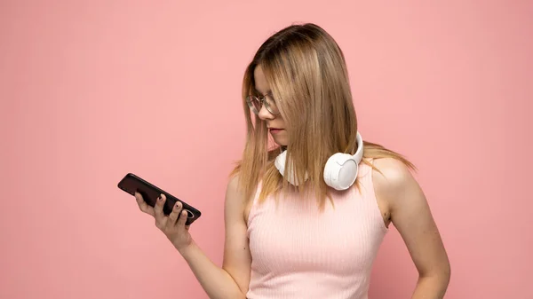 Jeune femme blonde dans un t-shirt rose et des lunettes en utilisant un téléphone et en envoyant un message ou en bavardant avec un ami dans des messagers. — Photo