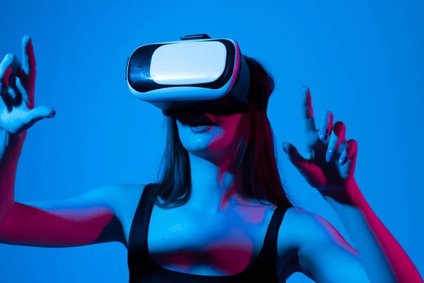 Lenyűgöző fiatal nő megérintette a levegőt a VR élmény alatt. A lány egy virtuális valóság headsetet használ neon fényben. A nő a virtuális valóság szemüvegével. — Stock Fotó