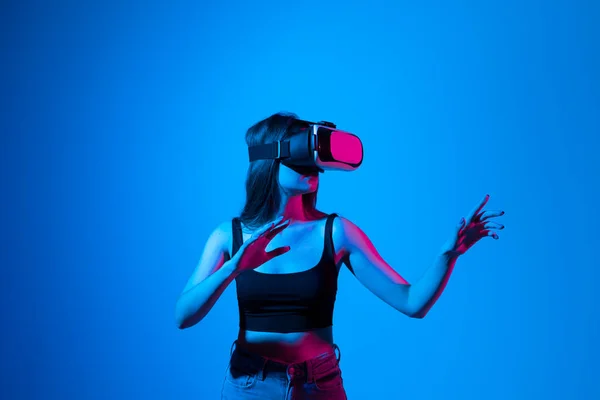 Brunetka ze słuchawkami VR dotykająca czegoś, co widzi w wirtualnym świecie. Technologia futurystyczna. — Zdjęcie stockowe