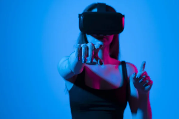 Mujer joven que usa gafas VR e interactúa con el ciberespacio usando gestos de deslizamiento y estiramiento mientras juega un videojuego con amigos en metáfora. — Foto de Stock