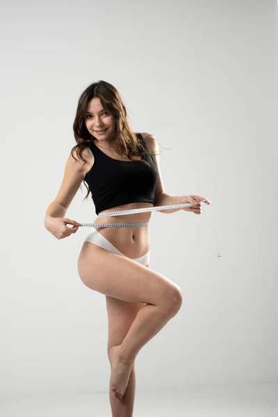 満足ブルネットフィットネス女性で黒上と白のショートパンツホールディング測定テープ周りに彼女の腰隔離された上の白の背景. — ストック写真