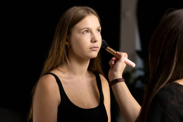 Makeup artist applying liquid tonal foundation on the face of the woman in make up room. Professional make-up artist working with brush on model face. — Stock Photo, Image