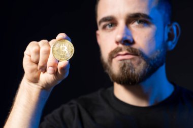 Siyah tişörtlü genç yakışıklı adam siyah arka planda izole edilmiş altın bitcoin gösteriyor..