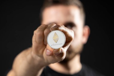 Stüdyoda gri arka planda izole edilmiş siyah tişörtlü başarılı bir iş adamı. Ethereum, bitcoin, gelecek para birimi.