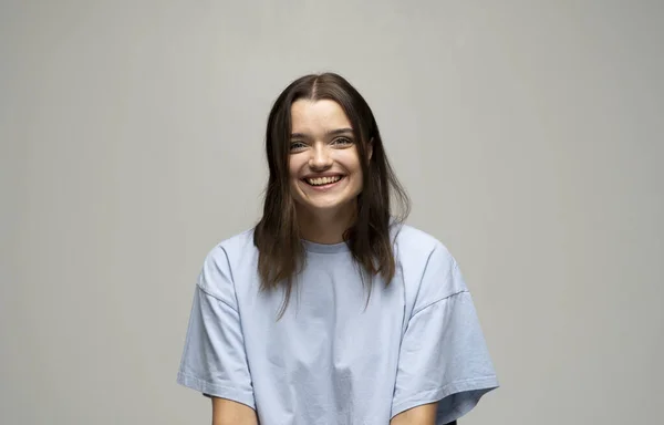 Gros plan portrait de la jeune femme brune émotionnelle en t-shirt bleu avec un grand sourire. Beau modèle posant en studio sur fond blanc. — Photo