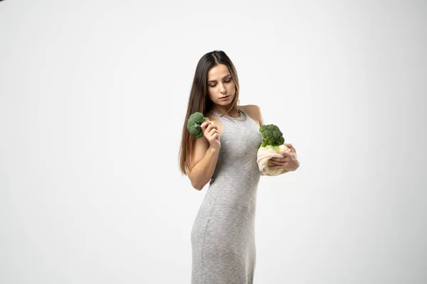 Jovem feliz segurando corda saco de malha reutilizável com legumes orgânicos. Mulher positiva em pé no fundo do estúdio verde. Eco amigável compras. — Fotografia de Stock