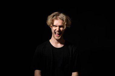 Siyah tişörtlü, vahşi genç adam siyah arka planda çığlık atıyor. Yüz ifadesi. Deli adam. Olumsuz duygular, sorunlar. Stresli adam bağırıyor..