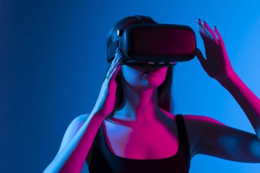 Genç bir kadın simülasyon oyunu oynamak için kulaklık kullanıyor. Sanal gerçeklik 3D video izliyor. VR gözlüklü kız etrafa bakıyor..