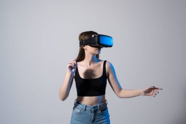 Genç bir kadın VR gözlük takarak stüdyoda duruyor ve ellerini sanal bir alanda kaydırıyor. Sosyal ağlardaki nesnelerle etkileşime geçiyor..