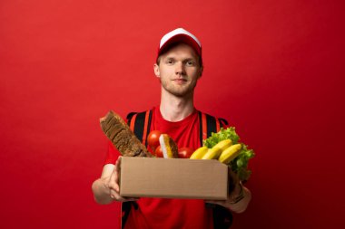 Kırmızı üniformalı teslimatçı ve termal çantalı karton kutuda beyaz arka planda izole edilmiş yiyecekler, stüdyo portresi var. Servis kavramı.