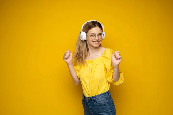 Hermosa joven rubia con auriculares escuchando música y sonriendo y bailando, aislada sobre fondo amarillo. —  Fotos de Stock