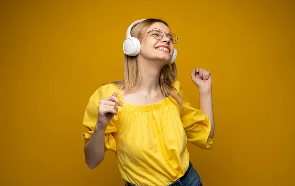 Красива молода блондинка в окулярах з навушниками слухає музику, посміхається і танцює, ізольована на рожевому фоні . — стокове фото