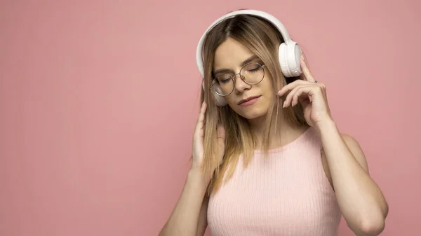 Joven rubia hermosa chica en gafas en traje rosa brillante disfrutando de una música sobre fondo rosa. —  Fotos de Stock