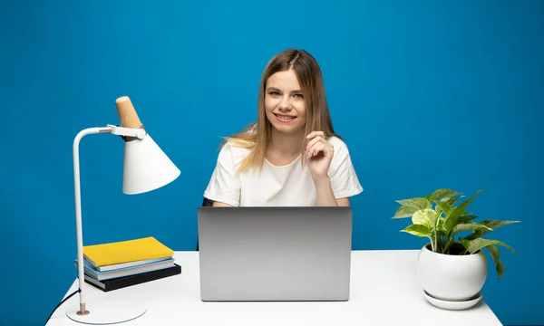 Retrato de uma jovem mulher bonita estudando enquanto se senta na mesa com computador portátil cinza, notebook. — Fotografia de Stock