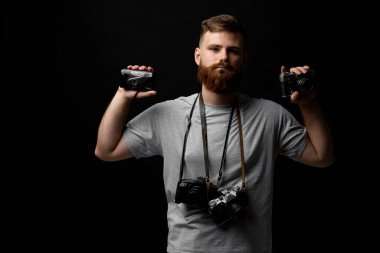 Profesyonel yakışıklı sakallı erkek fotoğrafçı. Fotoğraf stüdyosunda bir sürü klasik fotoğraf makinesi var. Siyah arka planda izole edilmiş..