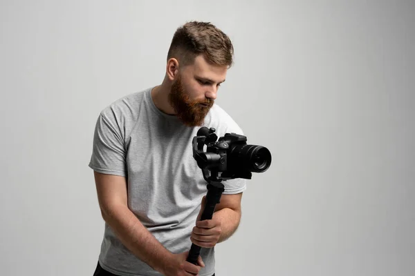 Filmmaking, hobby y concepto de creatividad. Videógrafo masculino profesional filmando vídeo usando una moderna cámara dslr en un gimbal de 3 ejes sobre una pared blanca. —  Fotos de Stock