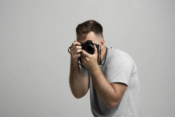 Jovem fotógrafo barbudo tira imagens com câmera dslr isolada no fundo branco. Trabalho freelance profissional, conceito de hobby e estilo de vida ativo. — Fotografia de Stock