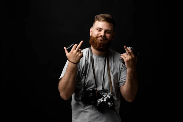 Fotógrafo masculino barbudo bonito profissional com um monte de câmeras de fotos vintage mostram um dedo médio com ambas as mãos no estúdio de fotos. — Fotografia de Stock