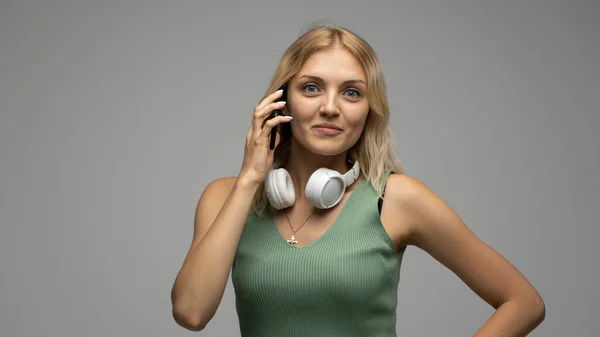 Foto de primer plano de la atractiva risita positiva joven rubia que se comunica en el teléfono móvil y sonríe aislada sobre fondo gris. —  Fotos de Stock