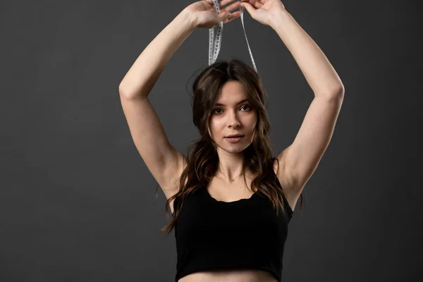 Brünette attraktive Frau in Unterwäsche blickt in eine Kamera und hält weißes Maßband um den Kopf. Gesundheitsversorgung und gesunde Ernährung. Perfekt schlanker Körper. — Stockfoto