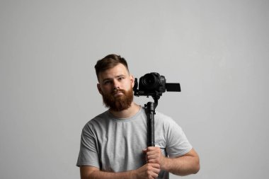 Film yapımı, hobi ve yaratıcılık konsepti. Profesyonel erkek görüntü yönetmeni, kameraman beyaz duvarın üzerinde 3 eksenli titreşimli modern DSR kamera kullanıyor..