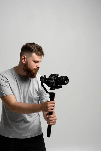 Επαγγελματική αρσενικό κινηματογραφιστής κινηματογραφιστής Dop γυρίσματα βίντεο χρησιμοποιώντας σύγχρονη κάμερα dslr σε 3-άξονα gimbal πάνω από λευκό τοίχο. — Φωτογραφία Αρχείου