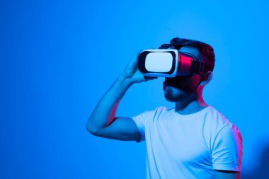 Modern stüdyoda neon ışığı olan sanal gerçeklik gözlüğü takan genç bir adamın yakın çekimi. Smartphone, VR kulaklığı kullanıyor. Gelecekteki teknoloji konsepti.