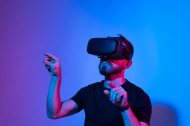 Sanal 3D gözlüklü bir adam neon ışıkta bir stüdyoda proje üzerinde çalışıyor. Adam video gözlüğü kullanarak arkadaşlarıyla video oyunu oynuyor..