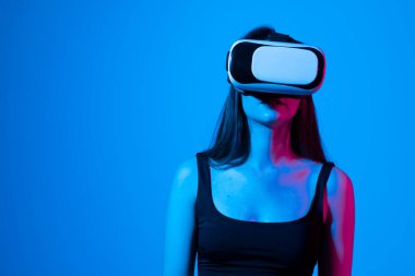 Modern cihazlar ve teknolojiler kavramı. Gelecekteki teknoloji konsepti. Mavi arka planda neon ışıklı VR gözlüklü genç kadın portresi. Sanal gerçeklik oyunu.
