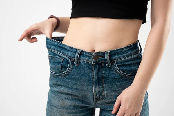 白い背景に体重減少の結果を示す青いオーバーサイズのジーンズの女性。ダイエットの概念と減量. — ストック写真