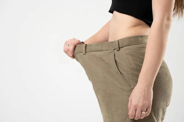 古い大きなジーンズを着てどれだけ体重を失うかを示す美しいスポーティ女性の側面図。国会の概念と体重減少。健康的なライフスタイル. — ストック写真