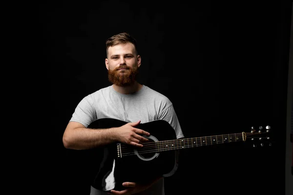 Портрет бородатого музиканта, гітариста, що стоїть і тримає акустичну гітару в руці і дивиться в камеру . — стокове фото