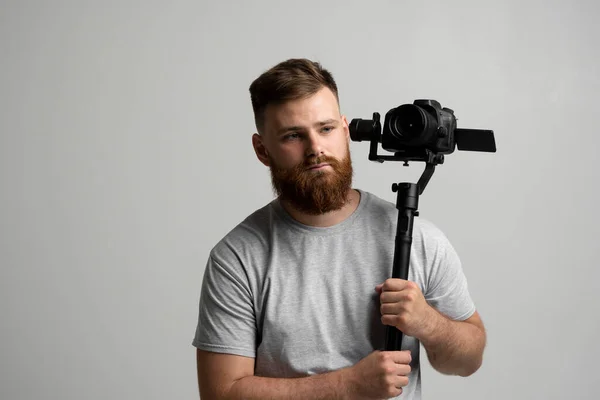 Profesjonalny brodaty fotograf trzymający kamerę, która ustawiona jest na 3-osiowym gimbale. Filmowiec korzystający ze Steadicama. Pro sprzęt pomaga w tworzeniu wysokiej jakości wideo bez wstrząsania. — Zdjęcie stockowe