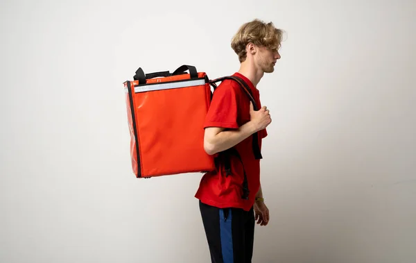 Dostawa Cocnept. Portret kuriera w czerwonym mundurze i torbie z termo plecakiem patrzącego na kamerę odizolowaną na białym tle studia. — Zdjęcie stockowe