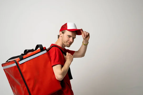 Widok z boku dostawca pracownik człowiek 20s w czerwonej czapce t-shirt jednolity termiczny torba żywności plecak pracy kurier service. — Zdjęcie stockowe