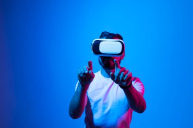 Heyecanlı sakallı bir adam sanal gerçekliği VR kulaklığıyla yaşıyor ve önünde gördüğü bir şeye elleriyle dokunuyor. Metaverse ve oyun.