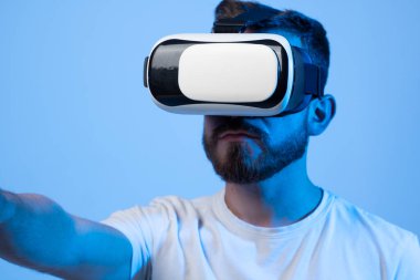 Genç adam simülasyon oyunu oynamak için kulaklık kullanıyor. Sanal gerçeklik 3D video izliyor. Gözlüklü sakallı adam etrafa bakıyor..