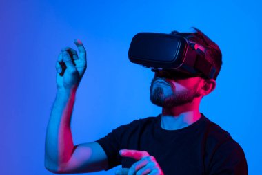 Sanal 3D gözlüklü bir adam neon ışıkta bir stüdyoda proje üzerinde çalışıyor. Adam video gözlüğü kullanarak arkadaşlarıyla video oyunu oynuyor..