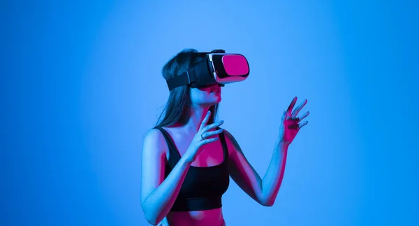Portret młodej kobiety bawiącej się w okulary VR w neonowym świetle na niebieskim tle. Koncepcja nowoczesnych gadżetów i technologii. Koncepcja technologii przyszłości. Gry wirtualnej rzeczywistości. — Zdjęcie stockowe