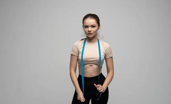 Esporte fitness atraente jovem morena em sportswear com fita métrica azul em seu ombro no fundo branco Esportes e dietas. — Fotografia de Stock