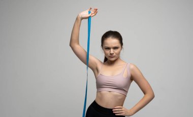 Kilo kaybı ve diyet kavramları. Spor kıyafetli çekici, zayıf esmer kadın elinde mavi bir mezura ile kameraya bakıyor. Sağlık ve sağlıklı beslenme.