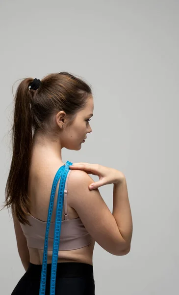 Costas de jovem bela mulher morena esportiva em roupa esportiva depois de treinamentos de aptidão com uma fita métrica azul em um ombro. Perda de peso e conceitos de dieta. — Fotografia de Stock