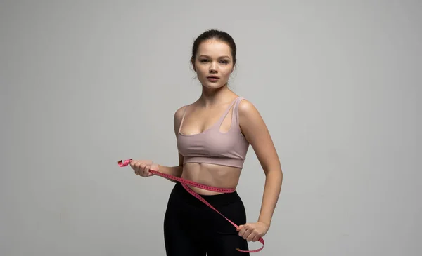 Attraktiva unga brunettkvinnor i sportkläder och mäter hennes midja. Mätningar av en kropp. Sport, fitness och kost. — Stockfoto