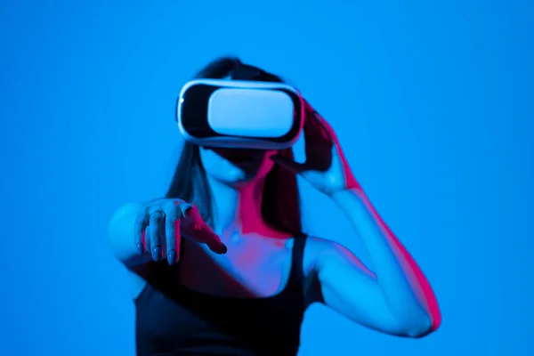 Chica alegre con las manos arriba usando las gafas de realidad virtual y jugando a un juego en luz de neón. Concepto de tecnología futura. Metaverso. — Foto de Stock