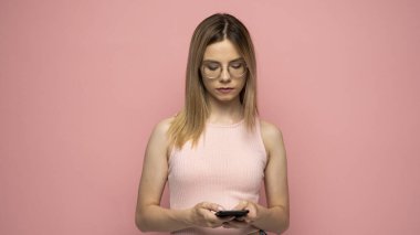 Pembe tişörtlü genç mutlu kız cep telefonu kullanıyor, pembe arkaplanda SMS mesajı yazıyor, stüdyo portresi çiziyor. İnsanların yaşam tarzı konsepti. Kopyalama alanı oluştur.